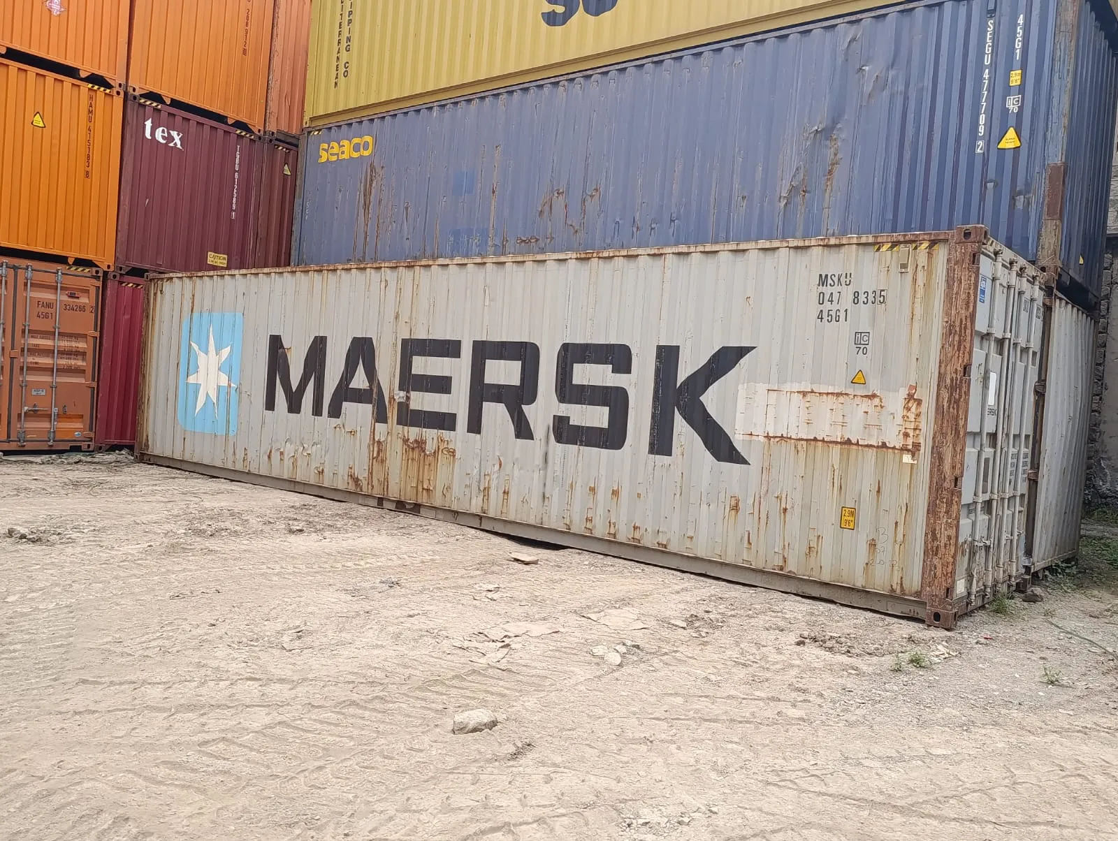 Used shipping container with stacked containers in the yard behind it